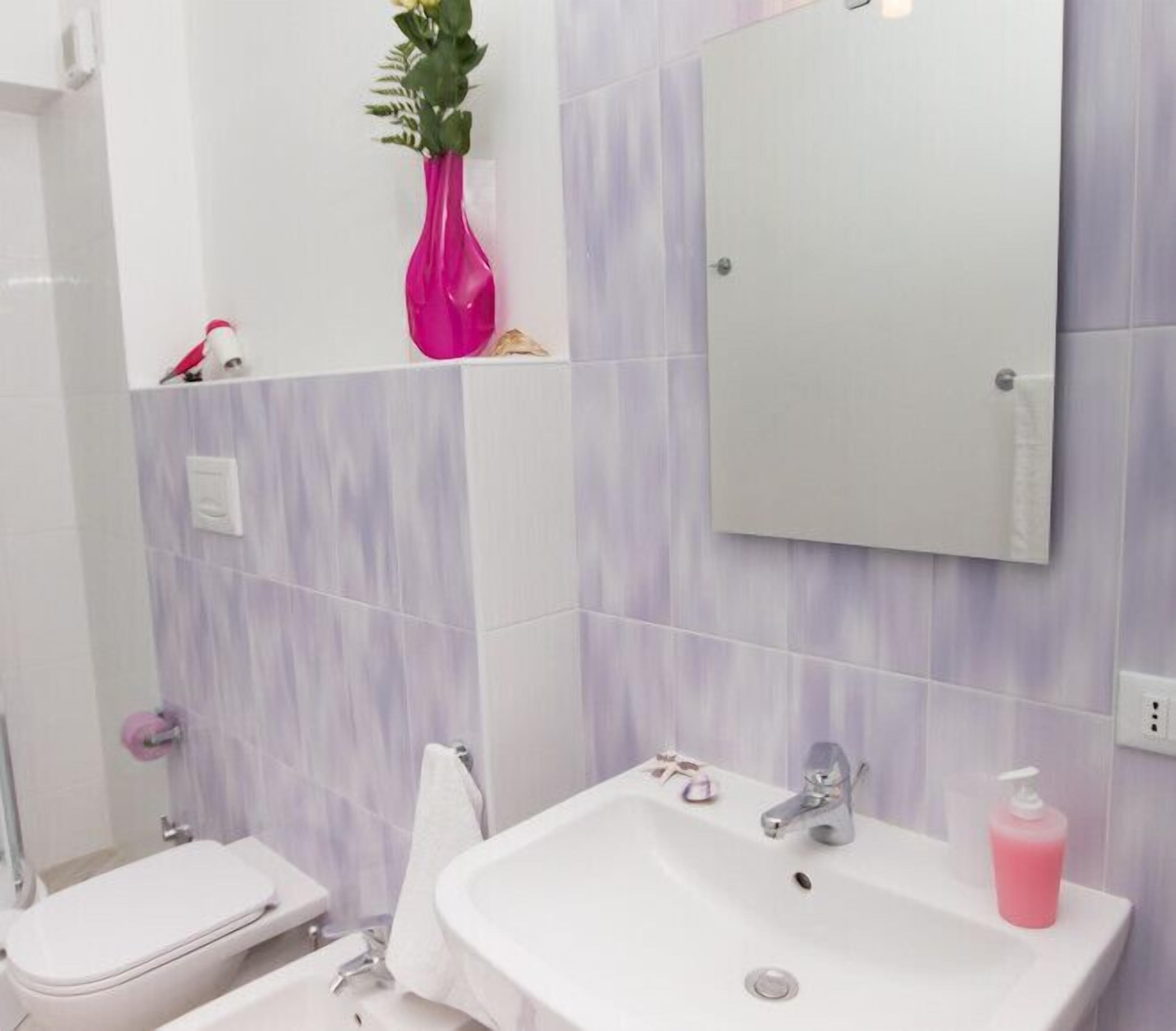 Une salle de bain avec un lavabo blanc, un miroir, un vase rose et des toilettes.