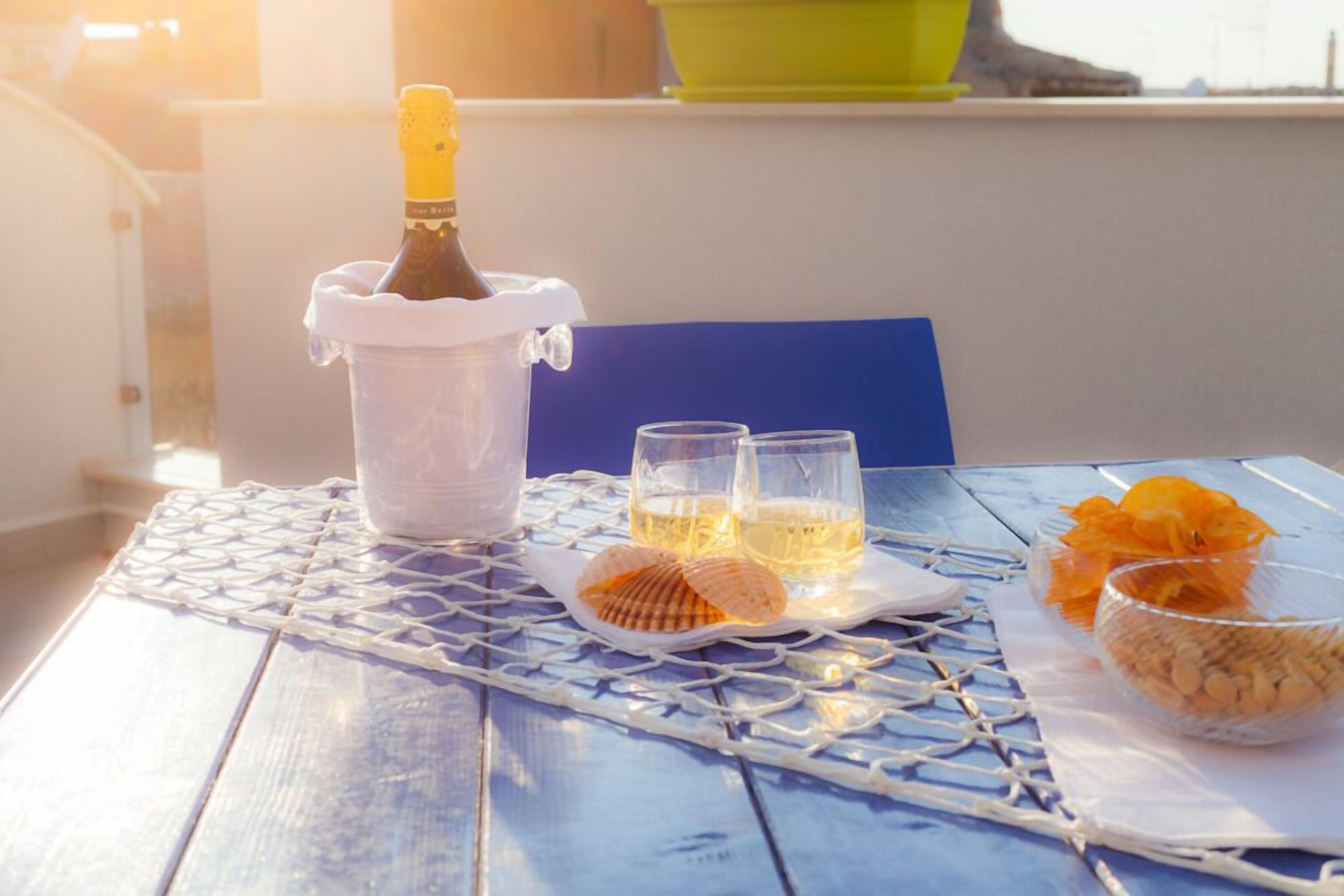 A table with a bottle of champagne, two glasses, a plate with snacks, and a bowl of fruit on a blue table with a white tablecloth.