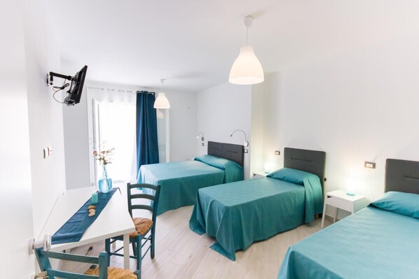 Habitación con dos camas, un escritorio y una silla. Se ve una ventana con cortinas, una mesa con un florero y velas, y un televisor instalado en el techo.