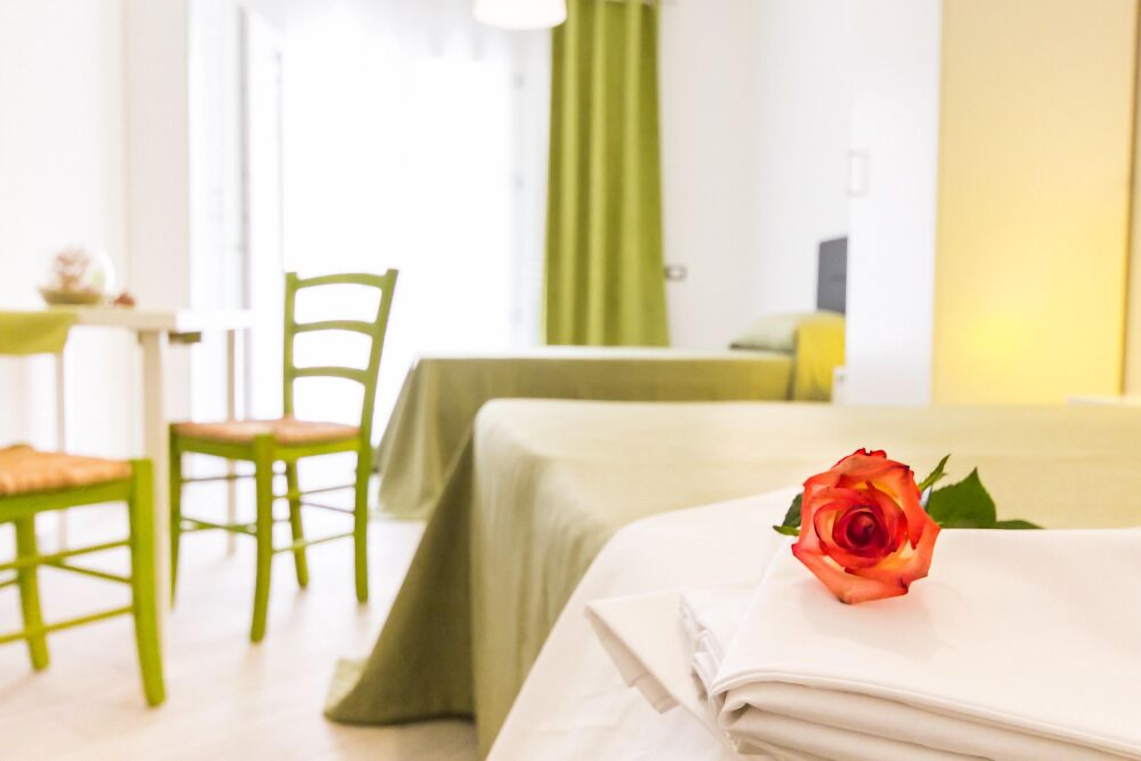 A hotel room with a neatly made bed, a green chair, and a table with a lamp.