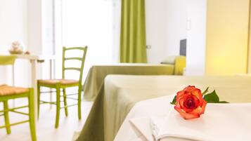 A hotel room with a neatly made bed, a green chair, and a table with a lamp.