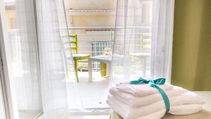 A room with a view of an outdoor balcony, a table with chairs, and a stack of towels on a table.