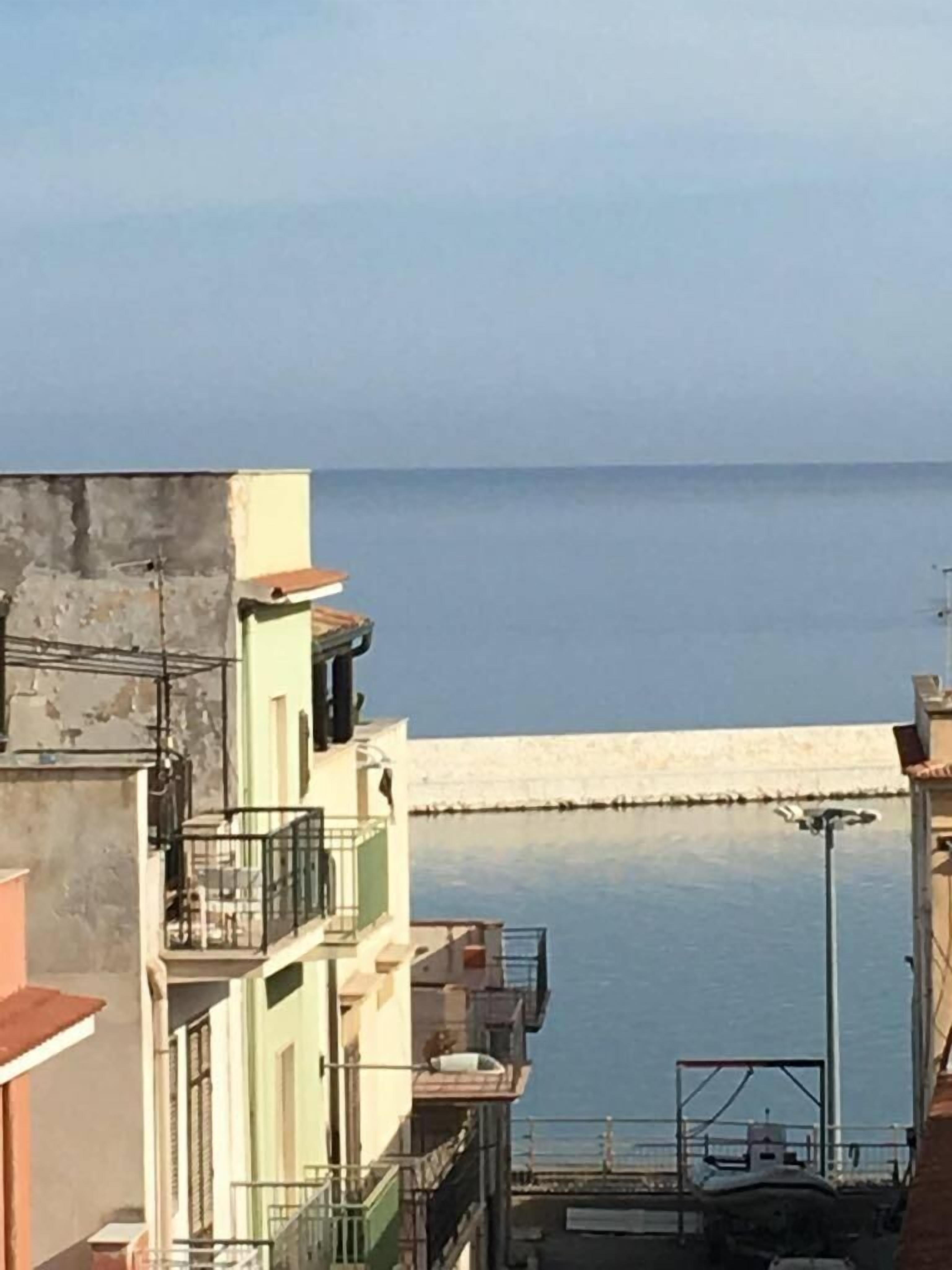 Una zona residencial costera con edificios cerca del mar, un muro de contención de hormigón y una vista despejada del agua.