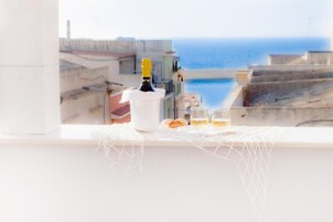 Una bottiglia di champagne, due calici e una conchiglia decorativa su un tavolo vicino a una finestra con vista sul mare.