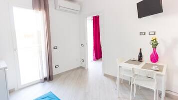 A bright, modern room with a white desk, two chairs, a flat-screen TV, and a window with curtains.