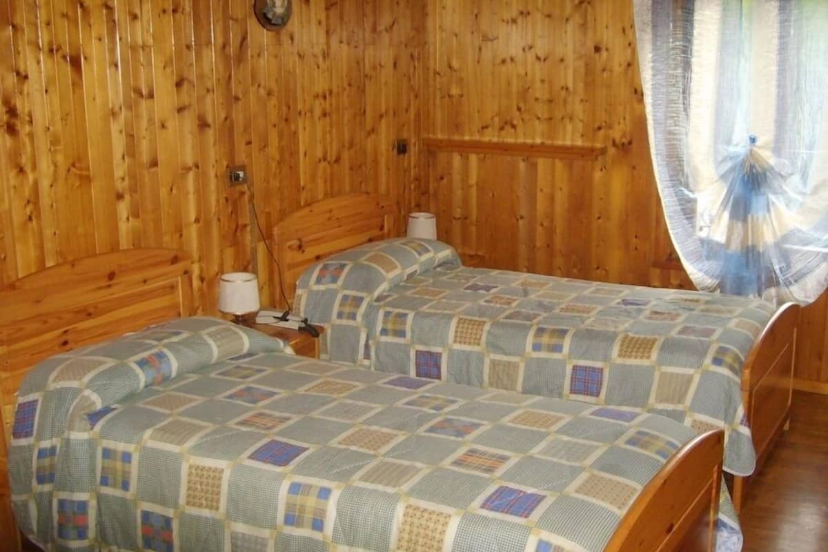Een kamer met houten lambrisering, twee bedden, een nachtkastje, een lamp en een wandlamp.