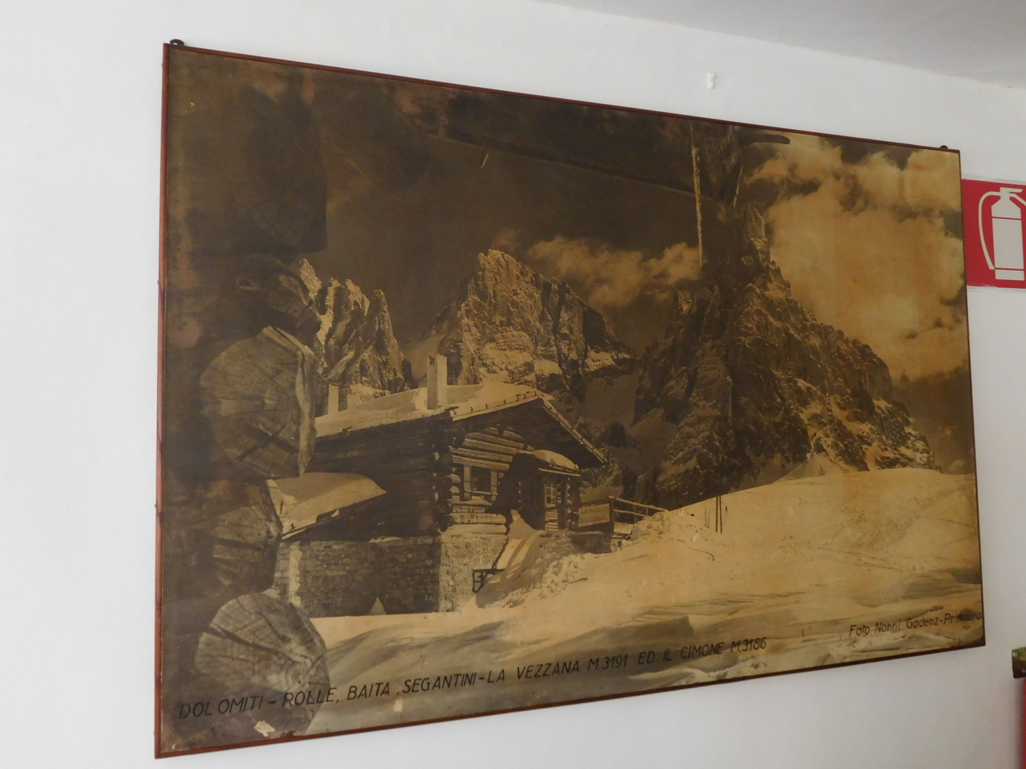 A vintage photograph of a mountain scene with a wooden cabin and a person in traditional attire.