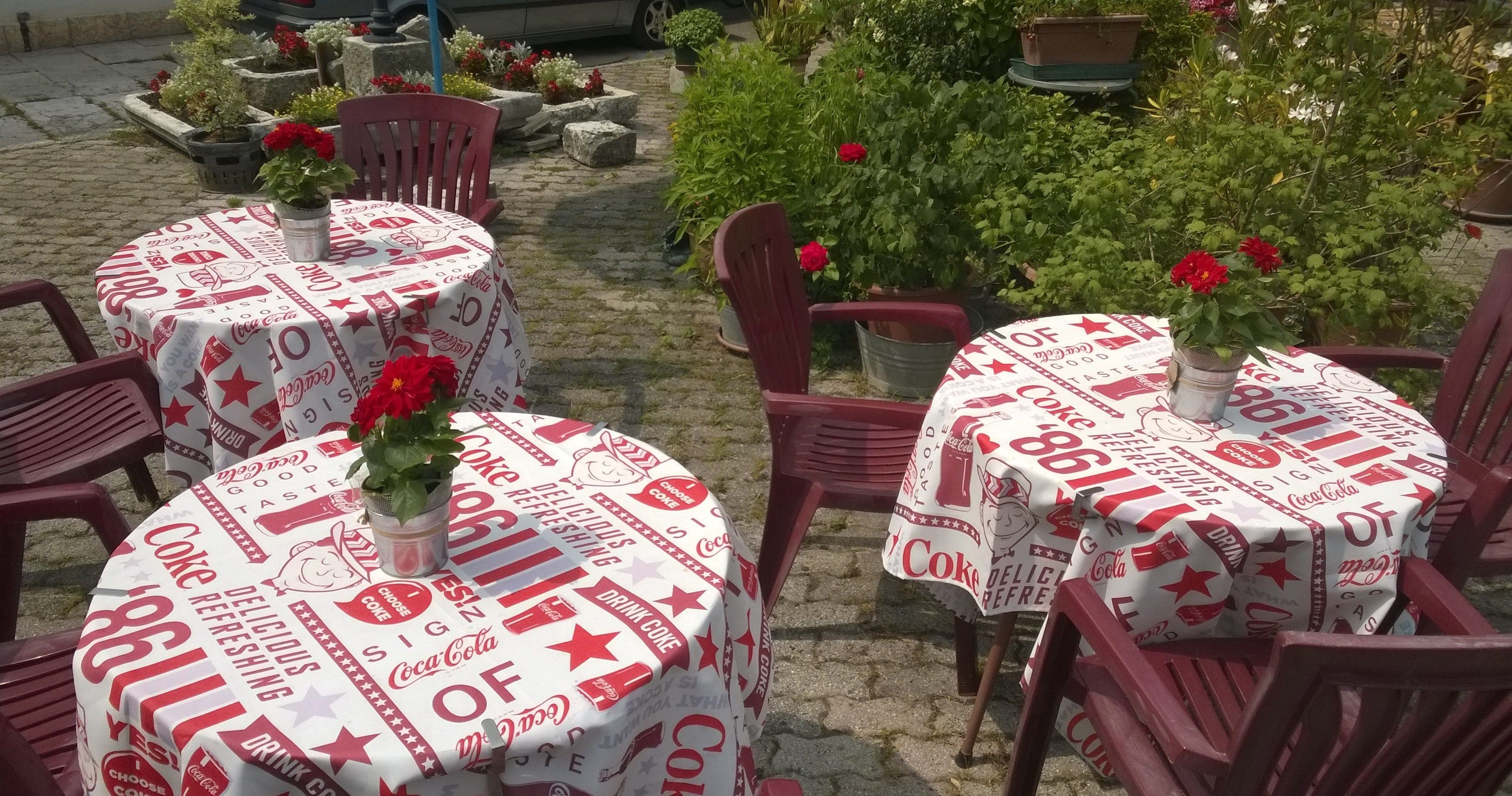 Tische im Freien, rund, mit Coca-Cola Tischdecken und roten Stühlen.