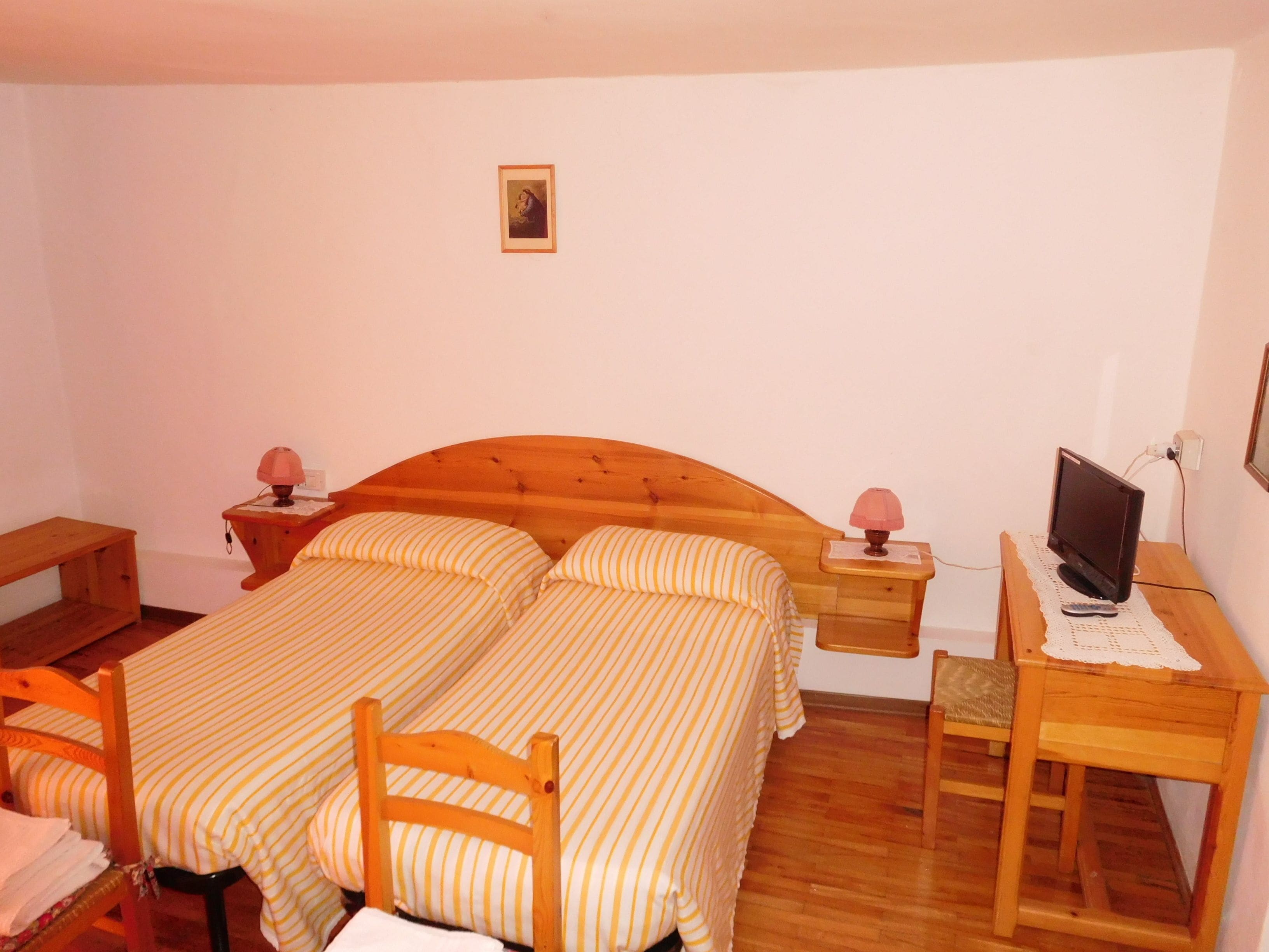 Een slaapkamer met twee bedden, een bureau, een stoel, een televisie en bedlampjes.