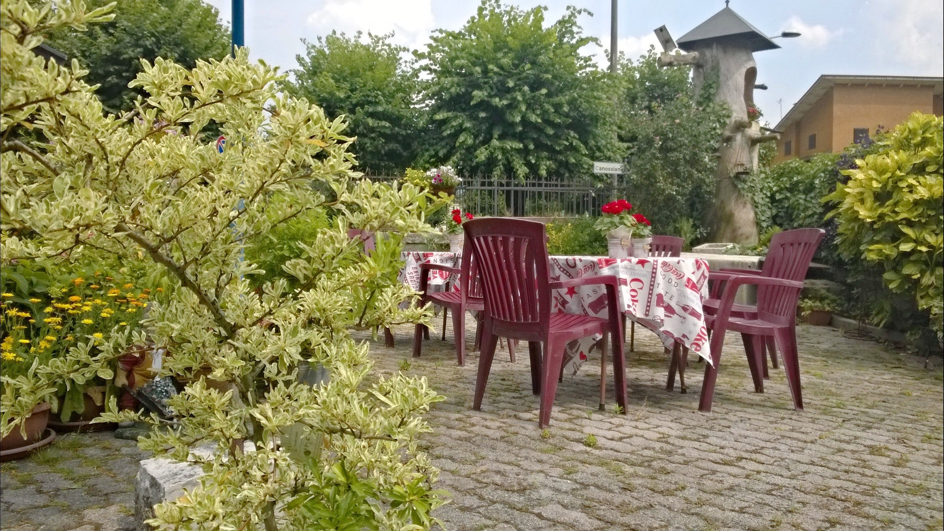An outdoor patio with a table and chairs, surrounded by potted plants and a stone pathway.
