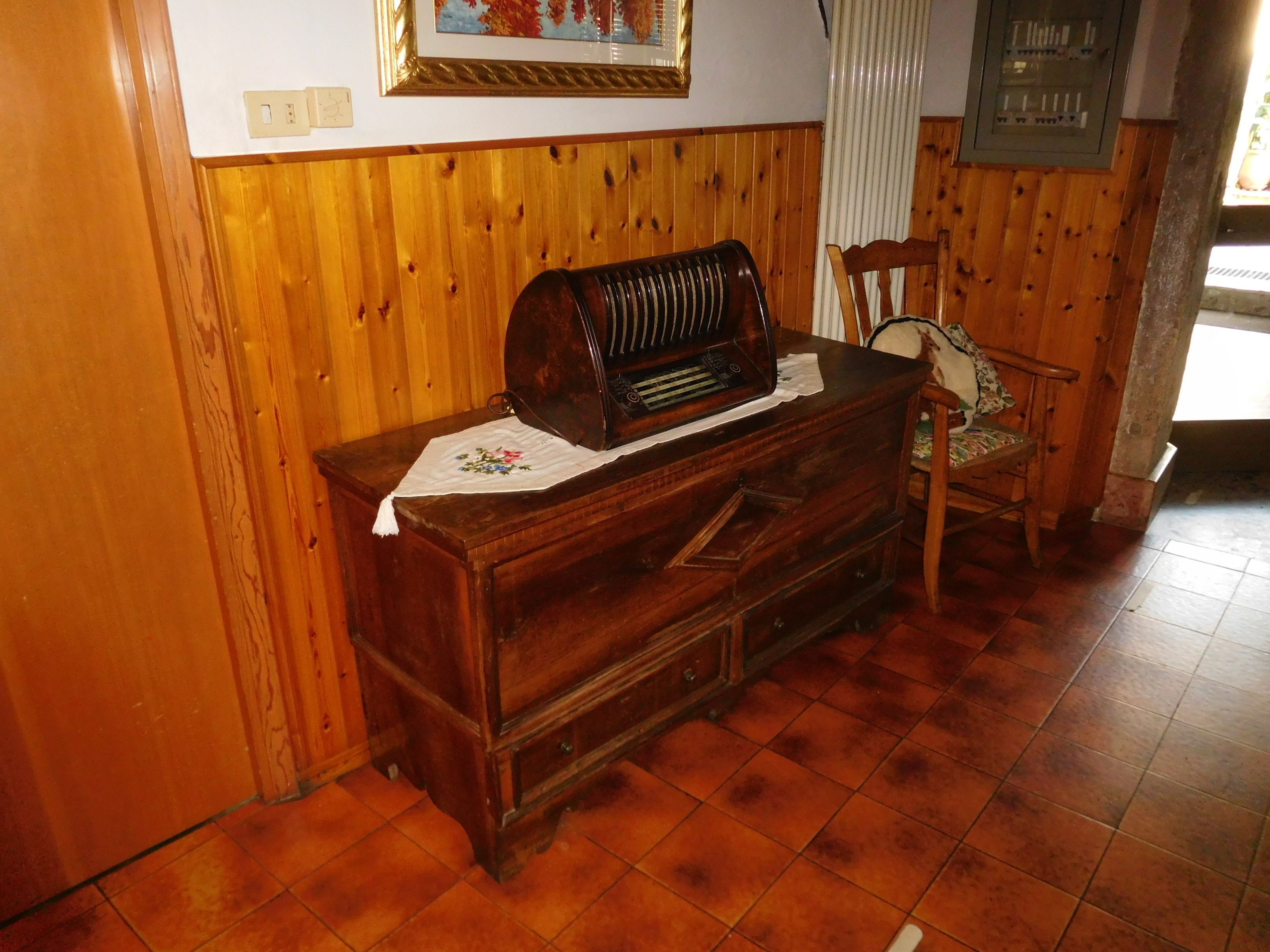 A wooden dresser with a radio, a chair, and a framed picture on the wall.