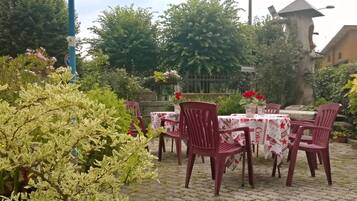 An outdoor seating area with tables and chairs, surrounded by greenery and a metal fence.