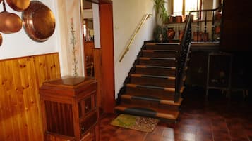 Una escalera de madera con barandilla que lleva a un rellano con una pequeña mesa y una planta en maceta.