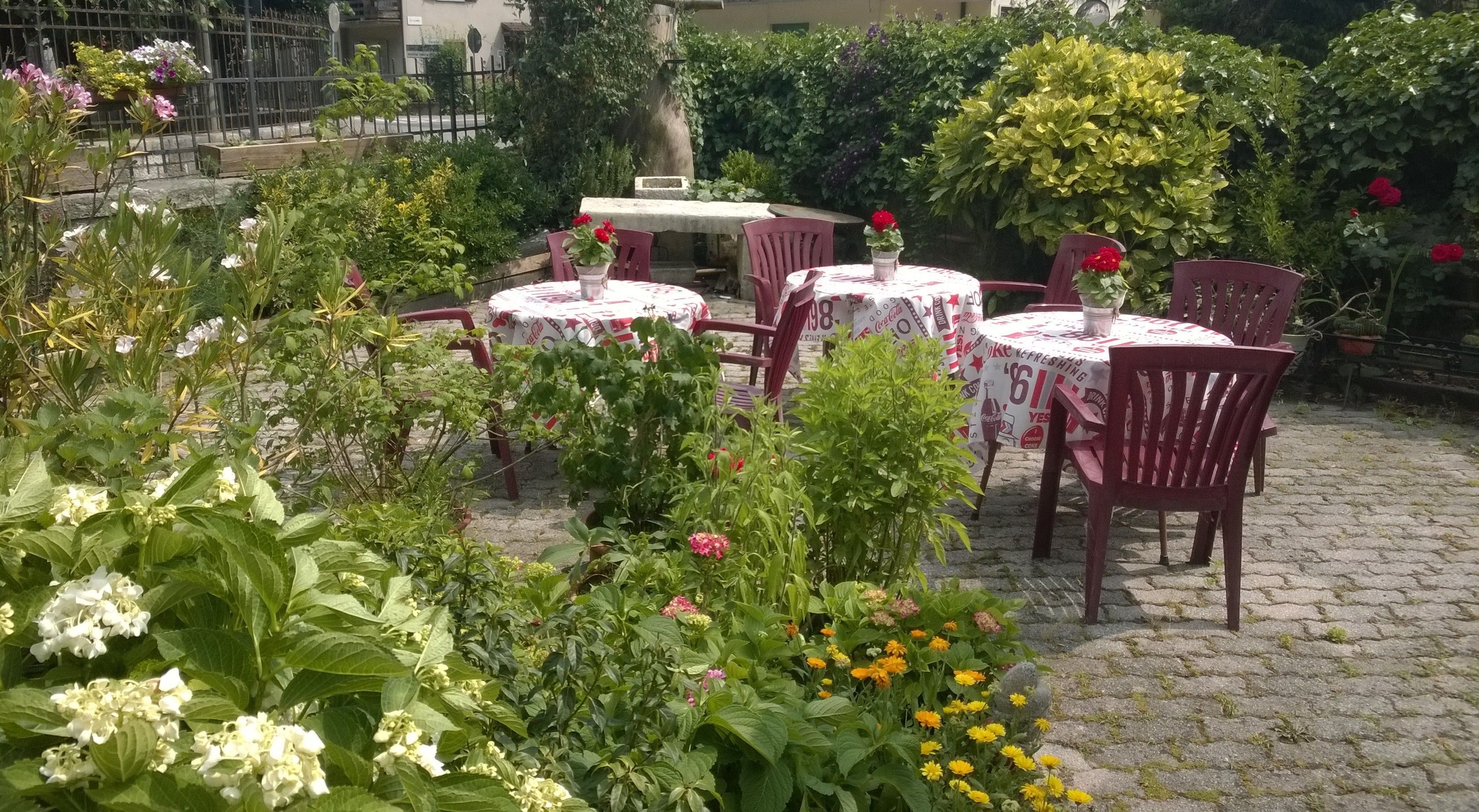 Ett utomhuskafé med bord och stolar, omgivet av frodig grönska och blommor.