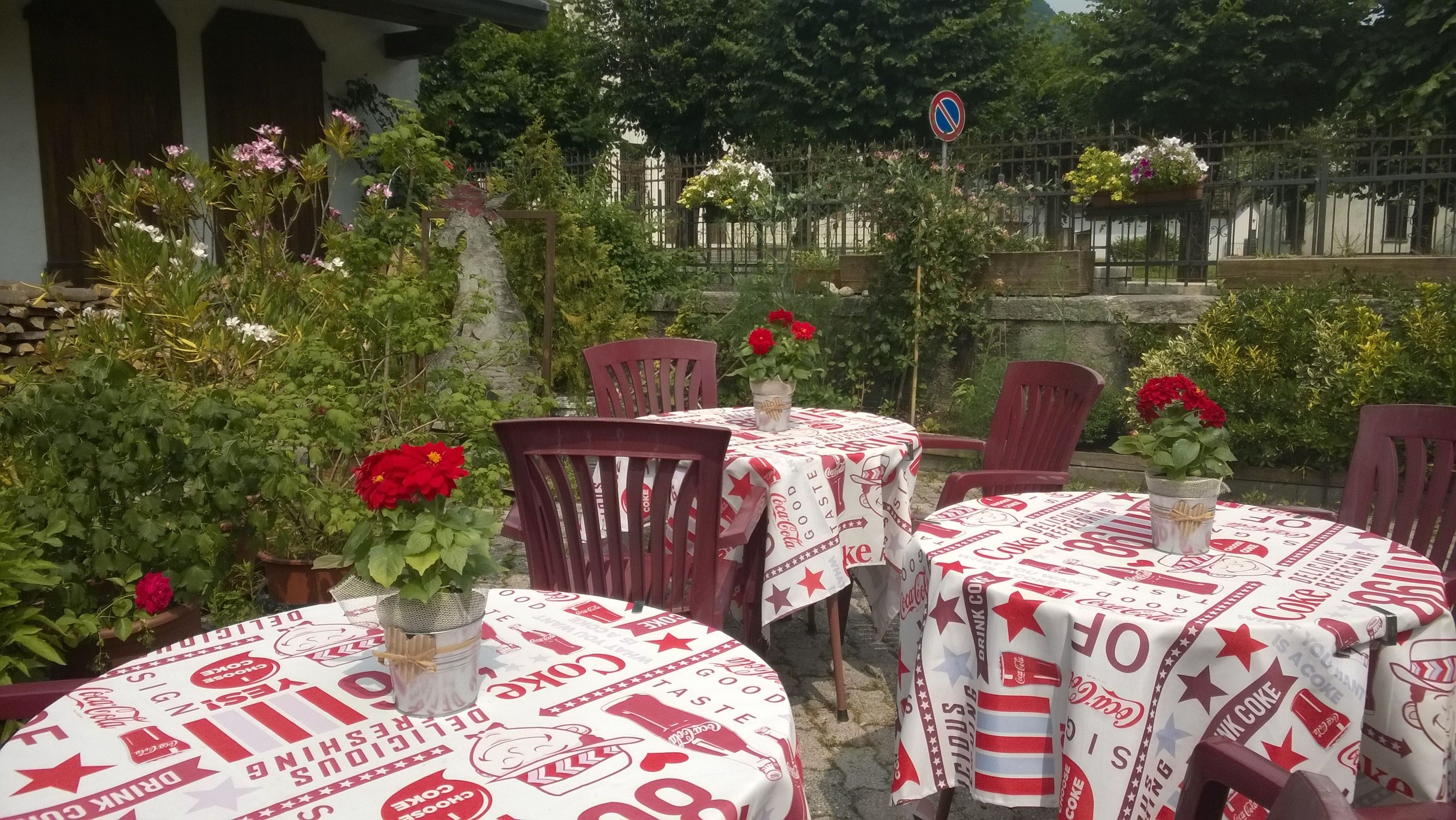 An outdoor seating area with tables covered in Coca-Cola branded tablecloths, surrounded by lush greenery and flowering plants.