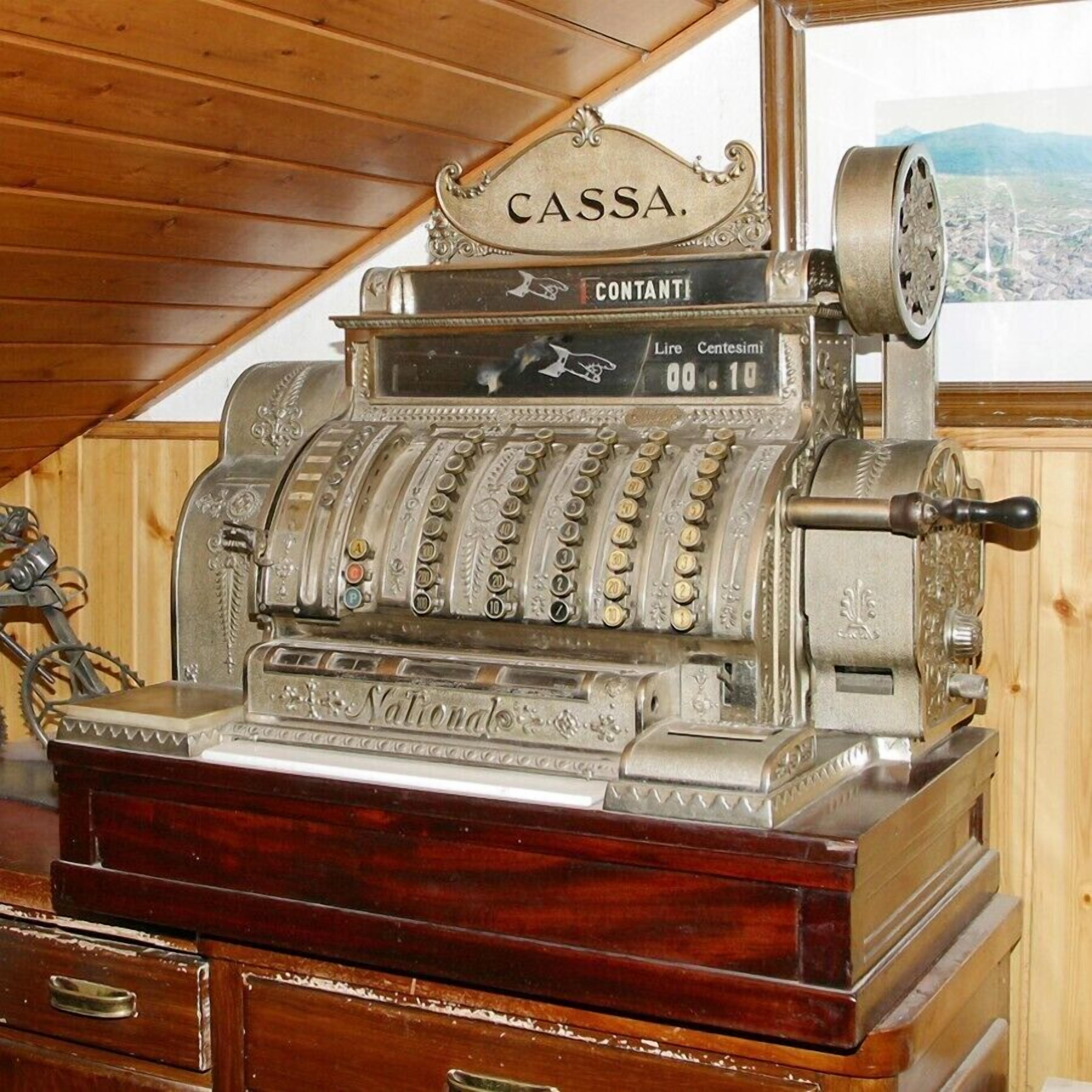An antique cash register with a wooden base and a sign that reads "CASSA CONTANTI".