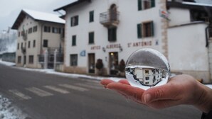 A hand holding a clear glass sphere reflecting a building with a sign reading "Alberida St. Antonis".
