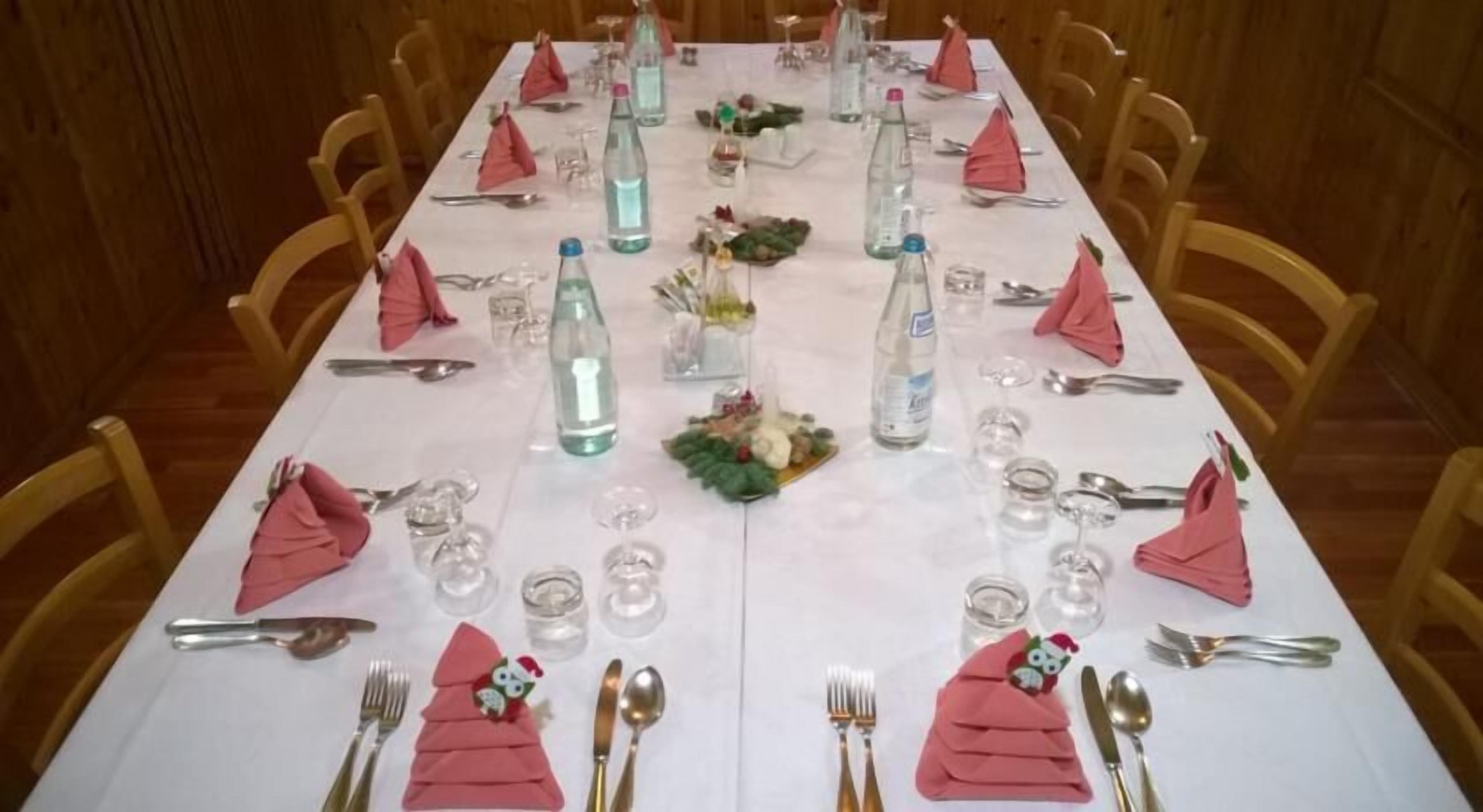 A long dining table set with pink napkins, silverware, and clear water bottles.