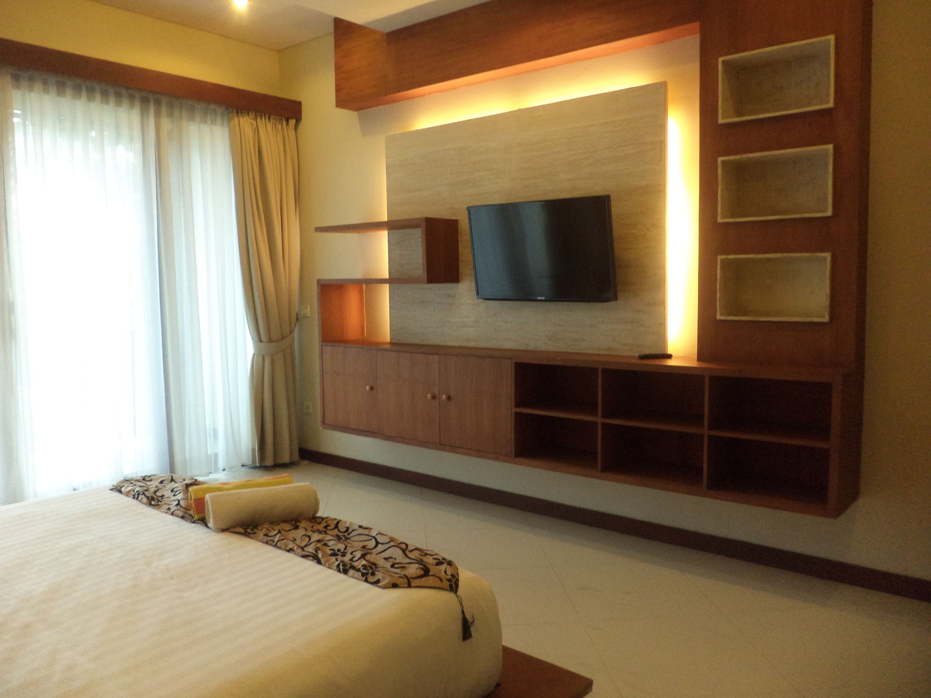 Quarto de hotel com uma cama grande, uma televisão de tela plana presa a um armário de madeira e uma janela com cortinas.