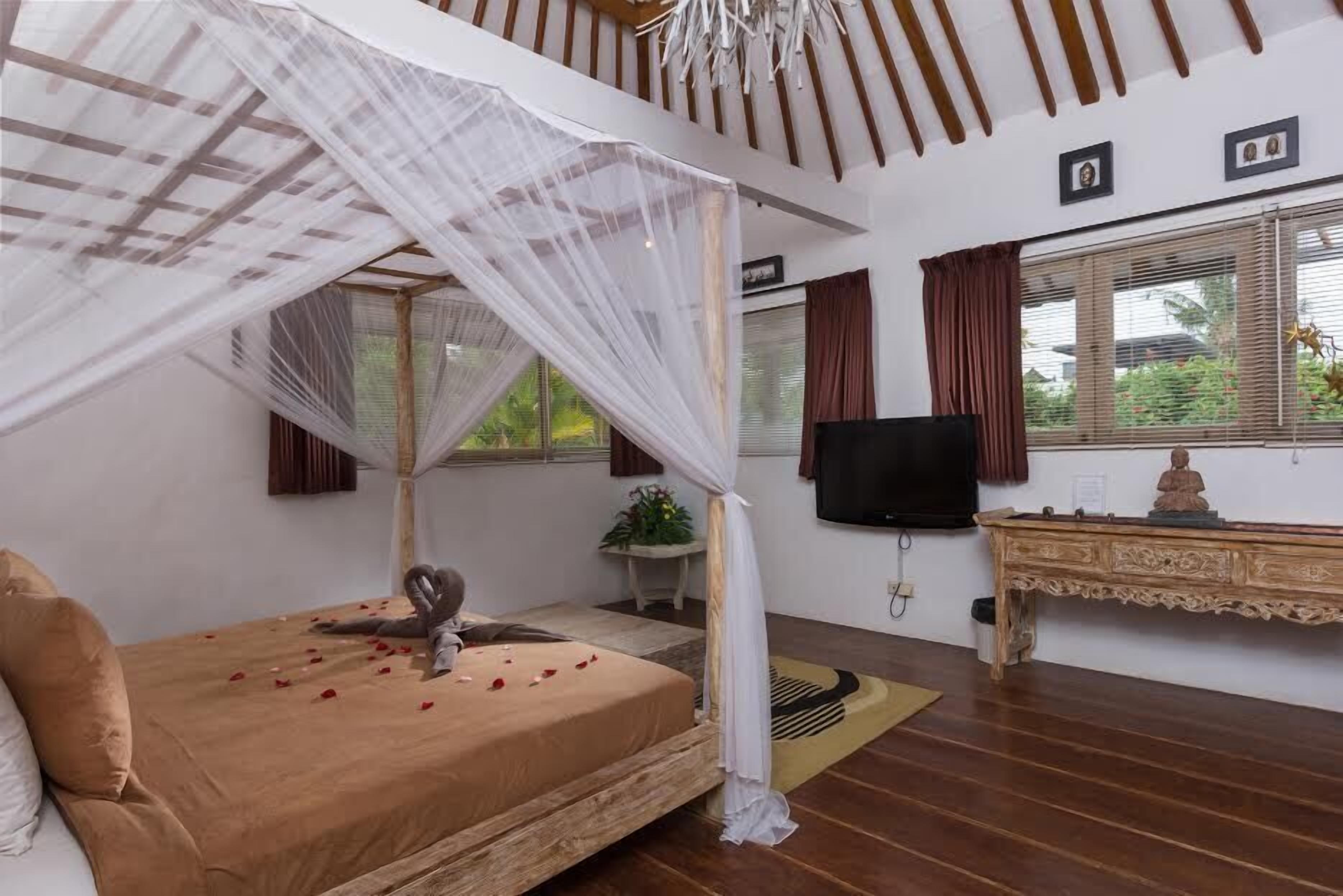 A bedroom with a canopy bed, a television, a small table with a statue, and a window with curtains.