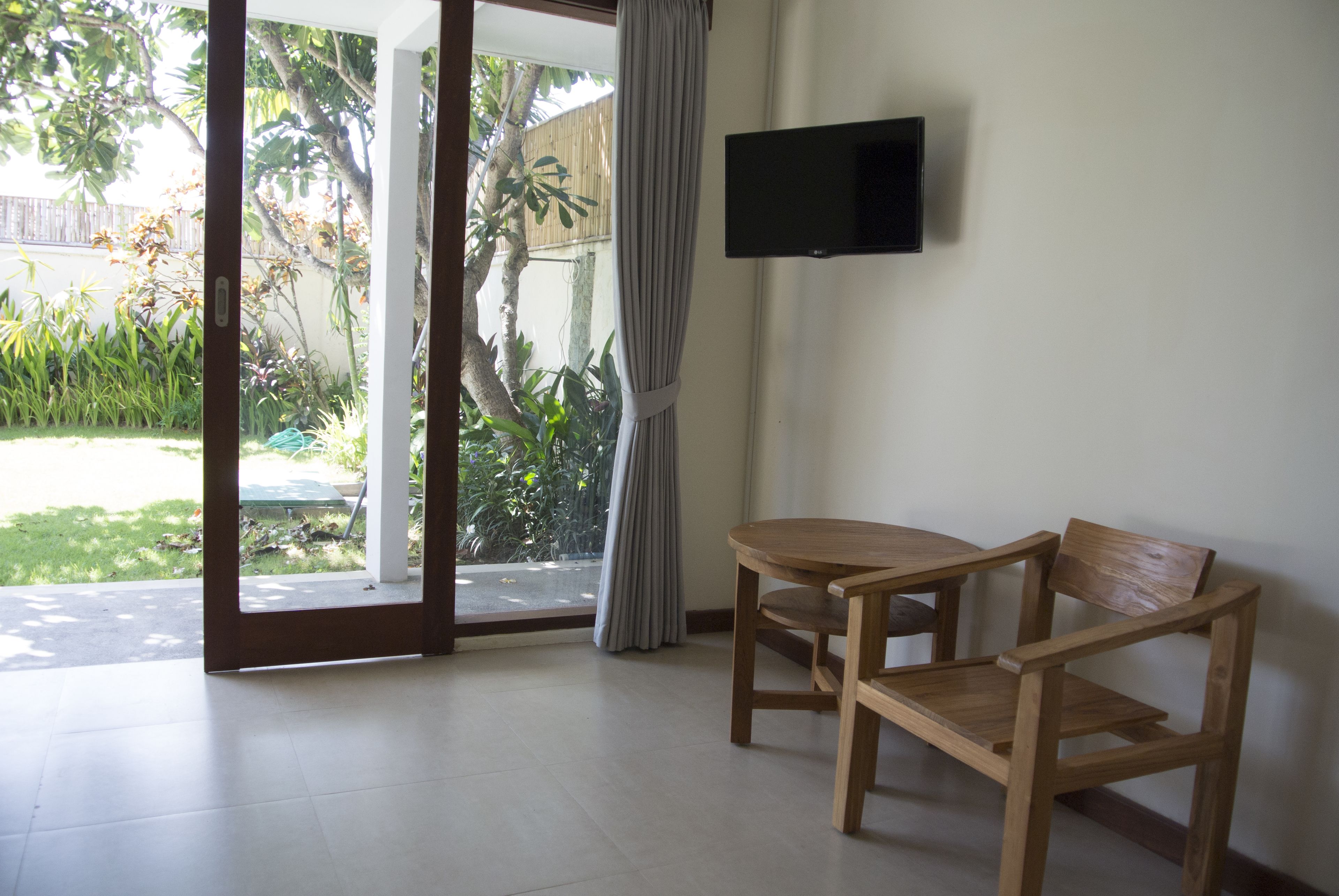 A room with a sliding glass door leading to a garden, a wooden table and chair, and a mounted TV on the wall.