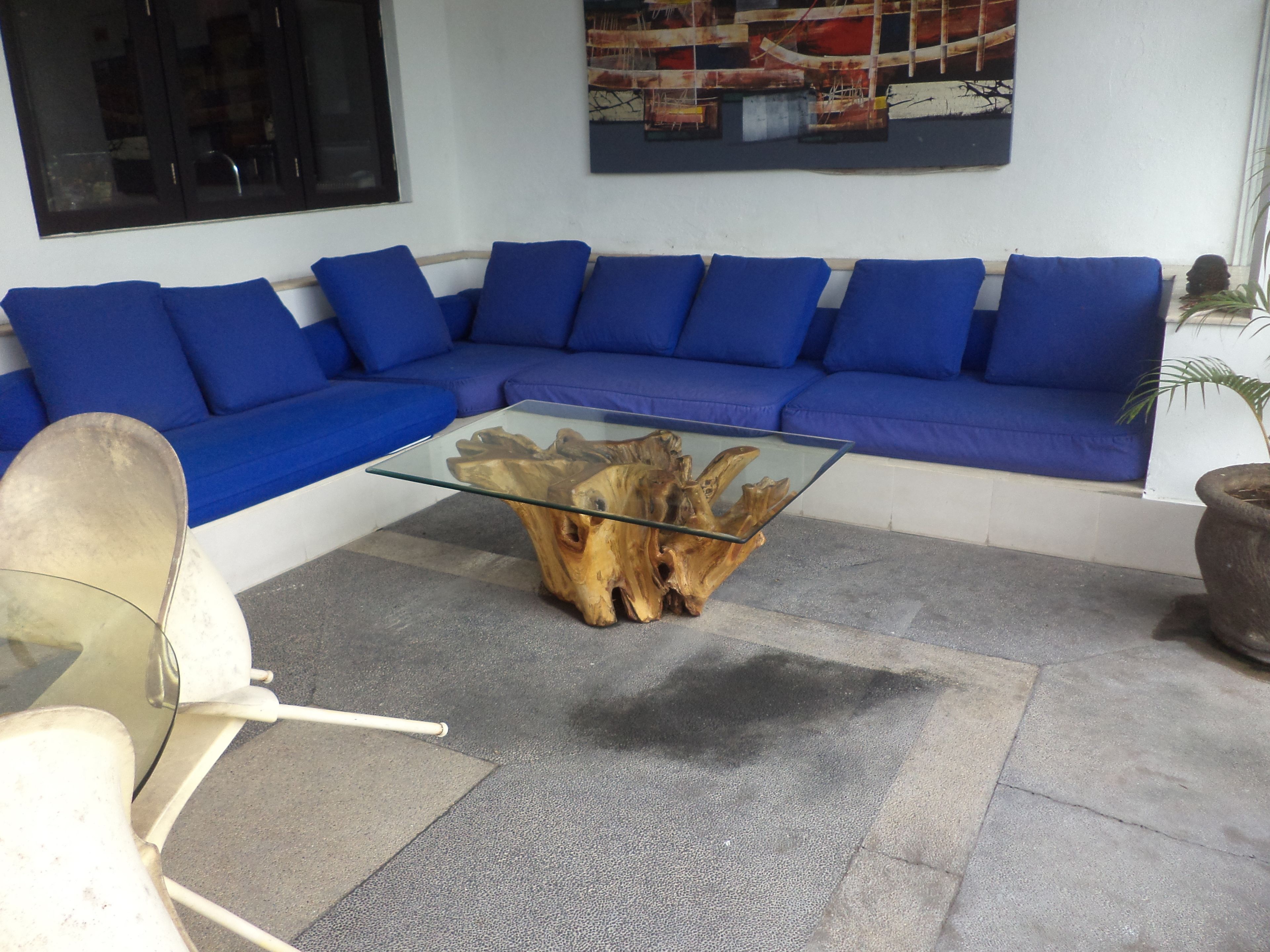 A modern living room with a blue sectional sofa, a glass coffee table with a wooden base, and a white chair.