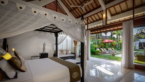 A bedroom with a canopy bed, a statue, and a view of a pool and garden. - Villa Dewi (Seminyak)
