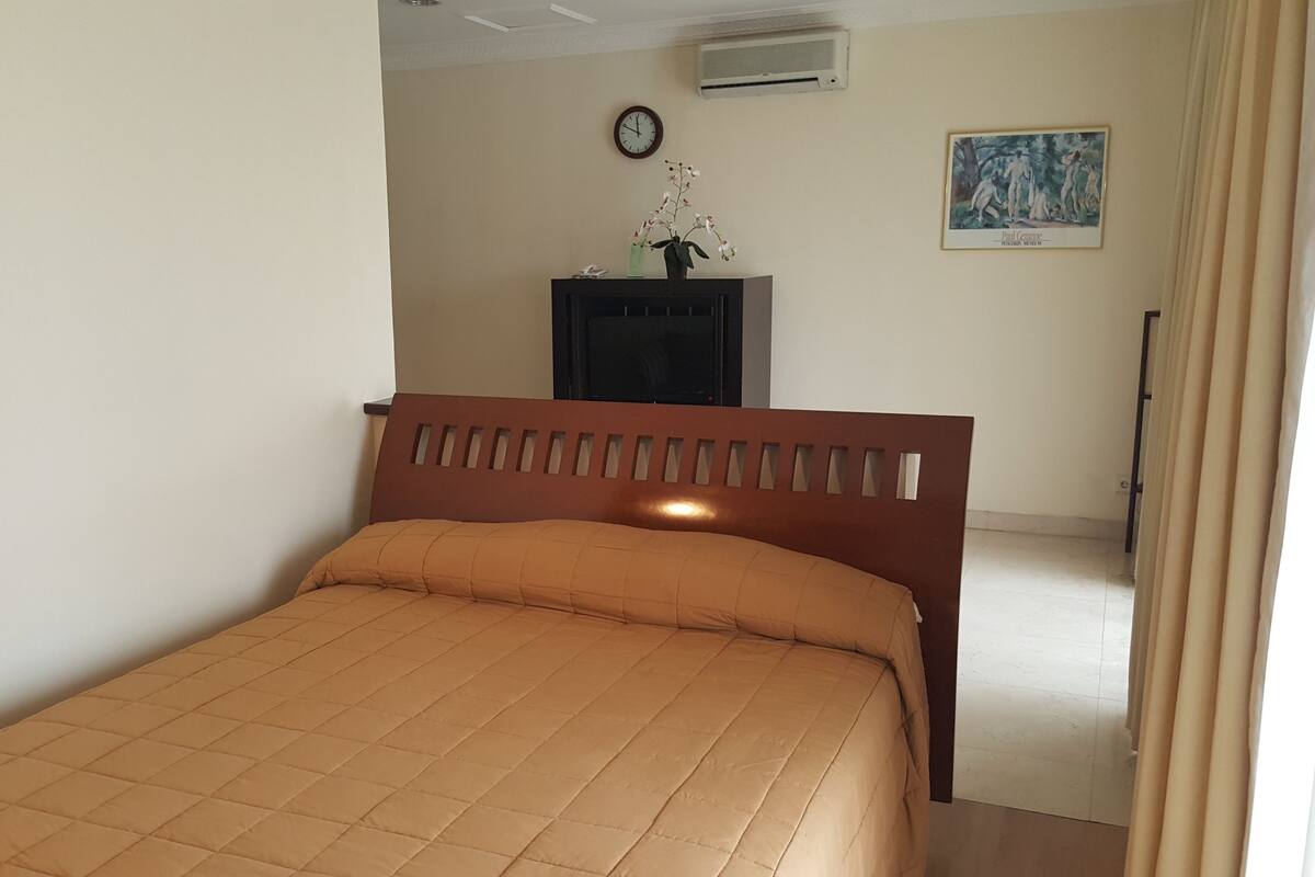 Un dormitorio con cama, un reloj, un cuadro enmarco y un aparador.