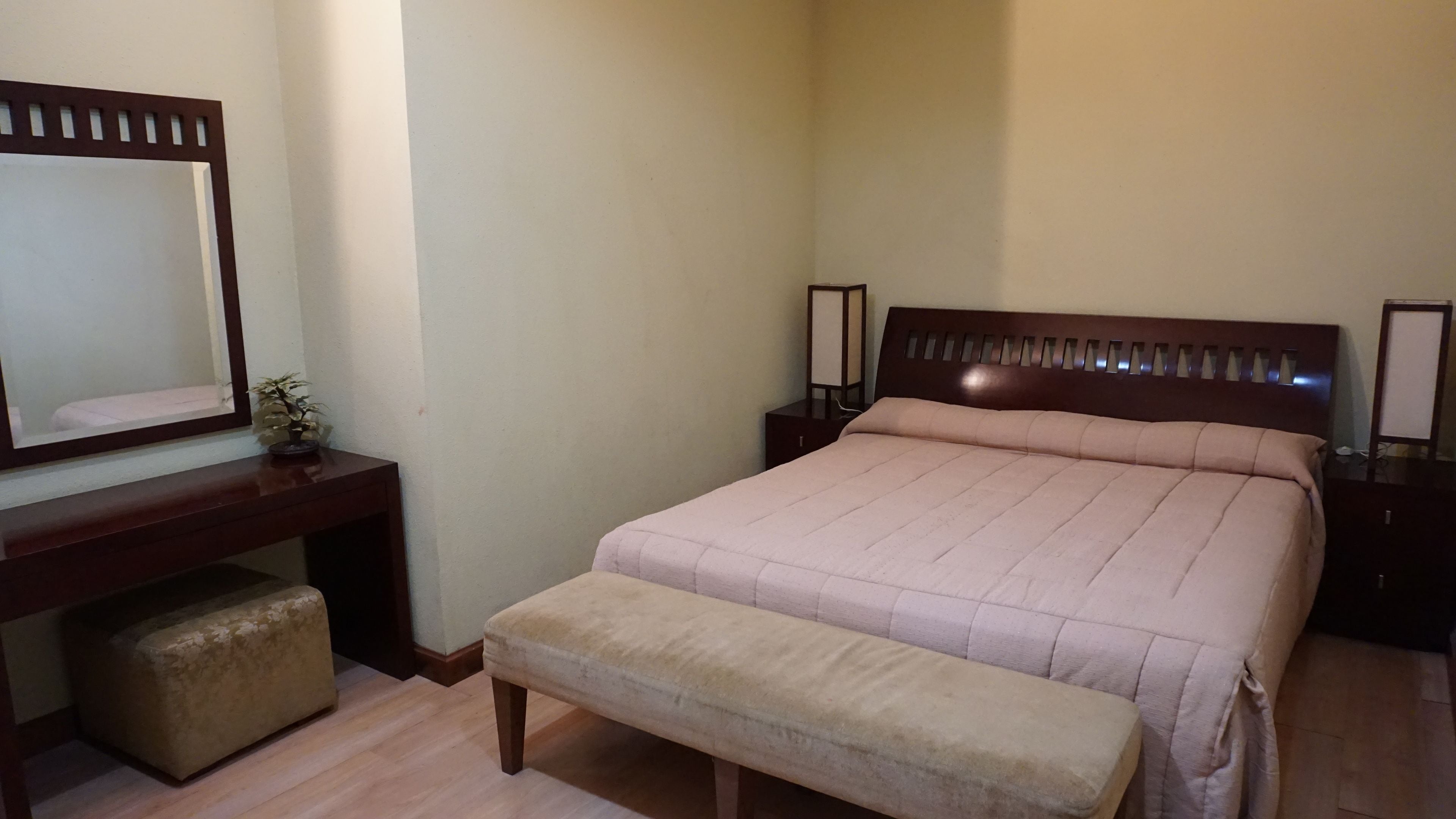 A bedroom with a bed, a bench, a nightstand, a dresser, and a mirror.