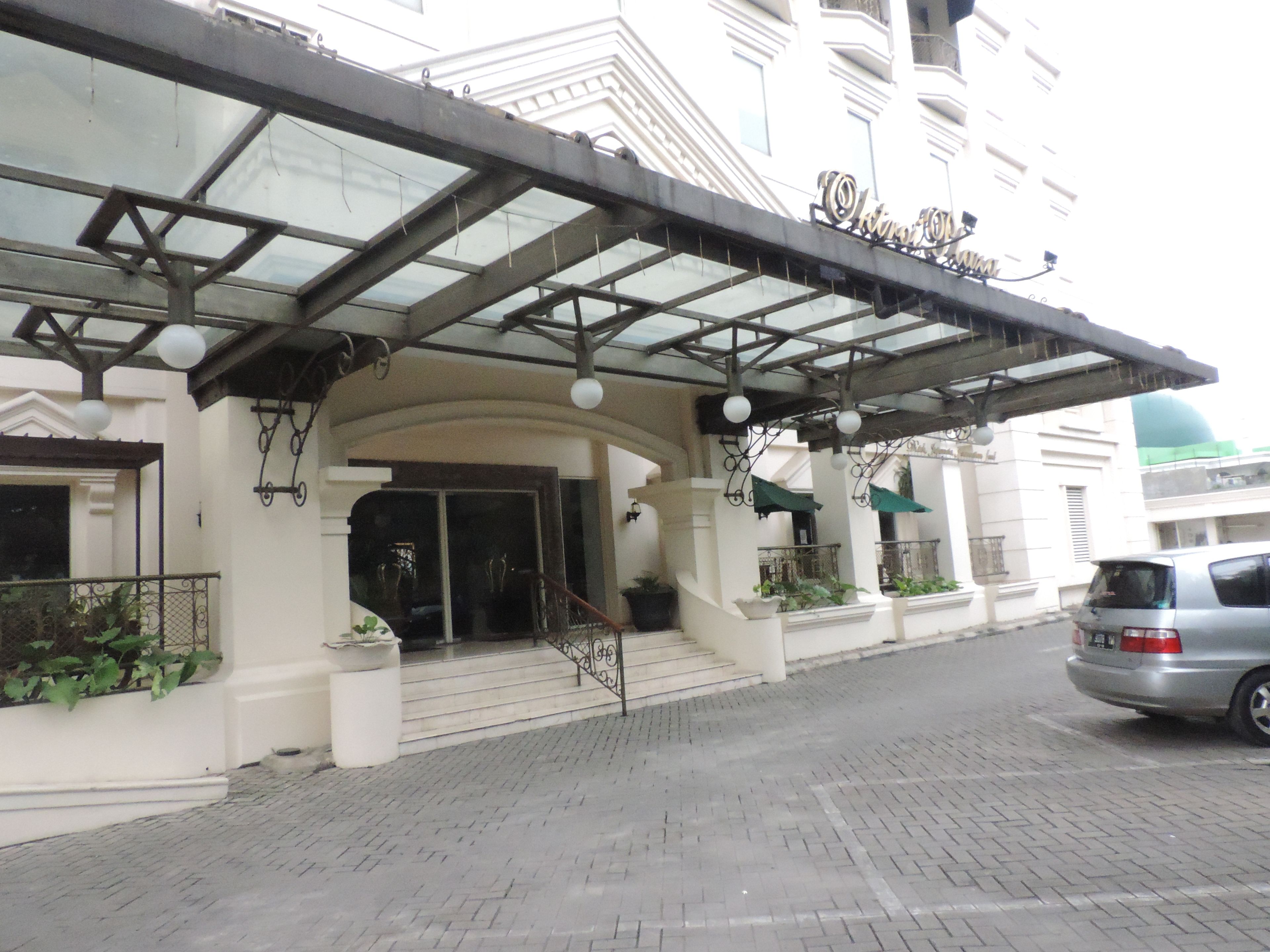 Entrada de hotel com galeria coberta, degraus até a entrada e vasos de plantas ao longo do caminho.