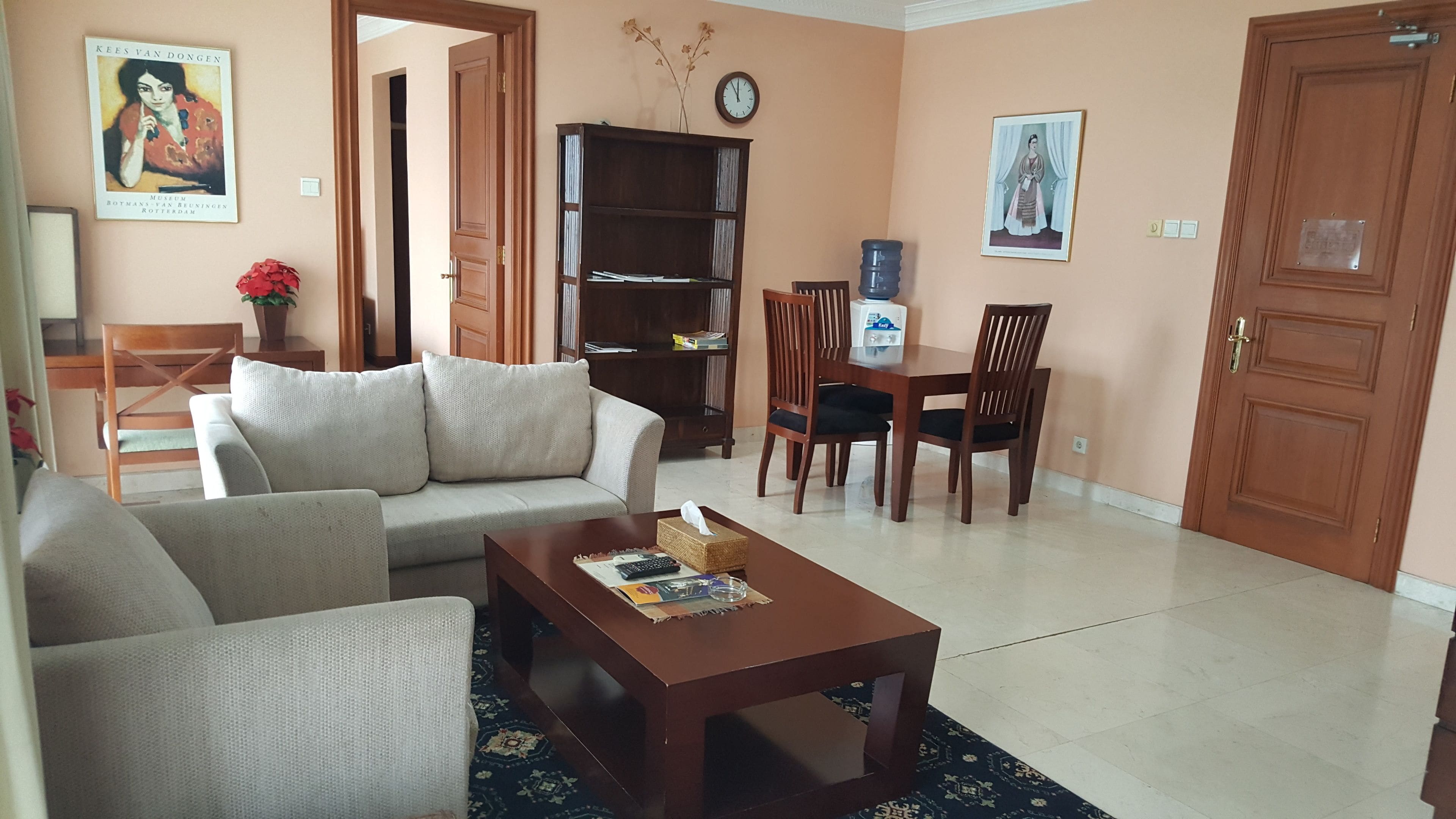 A living room with a sofa, a coffee table, a bookshelf, and a dining area with chairs and a table.