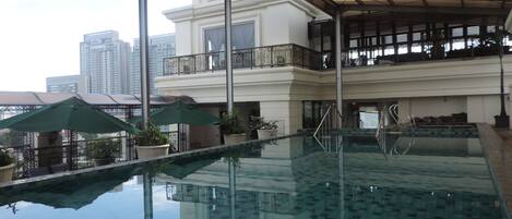 An indoor swimming pool with clear water, surrounded by potted plants and umbrellas.