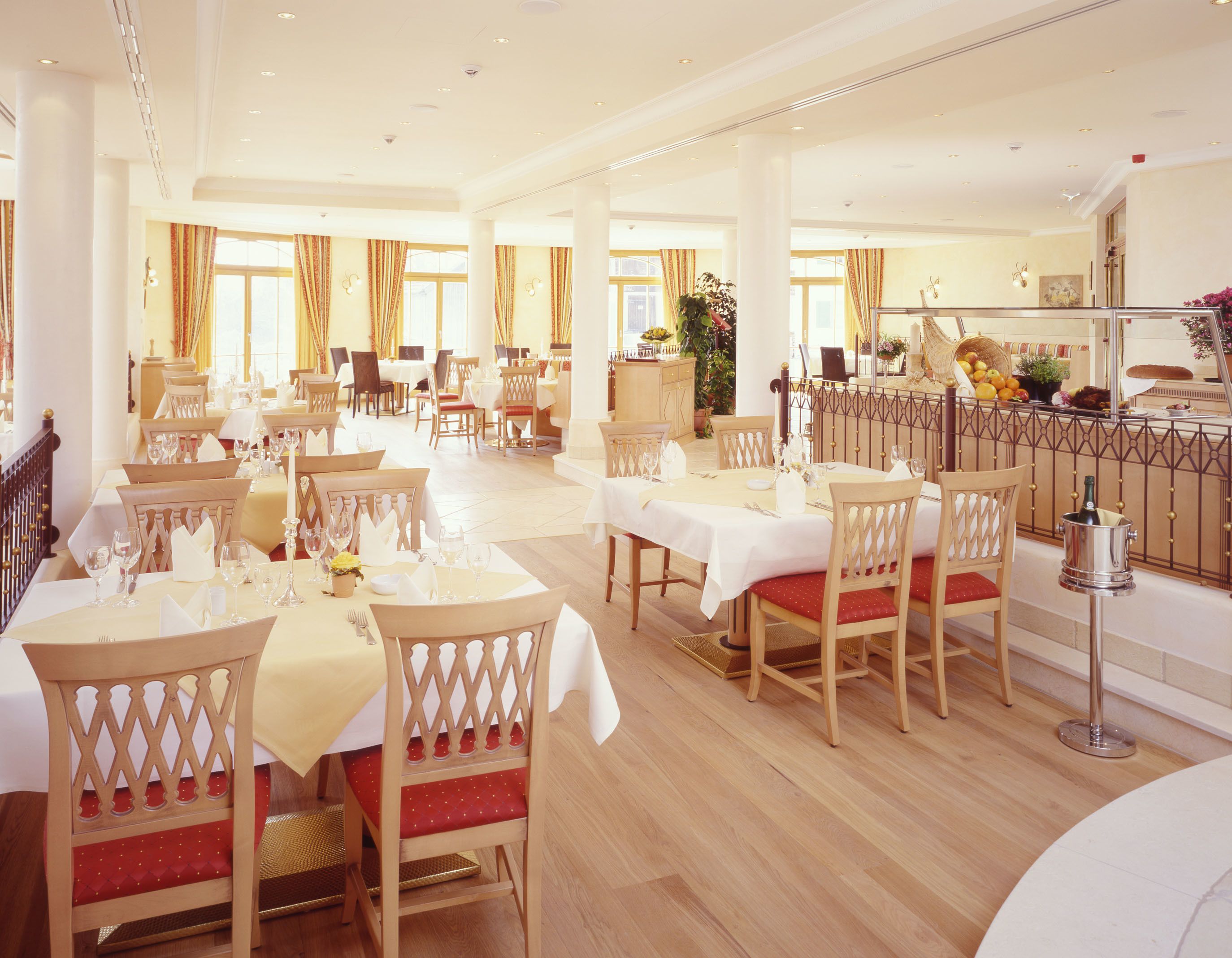 A spacious dining area with multiple tables and chairs, a decorative railing, and a view of the adjacent room.
