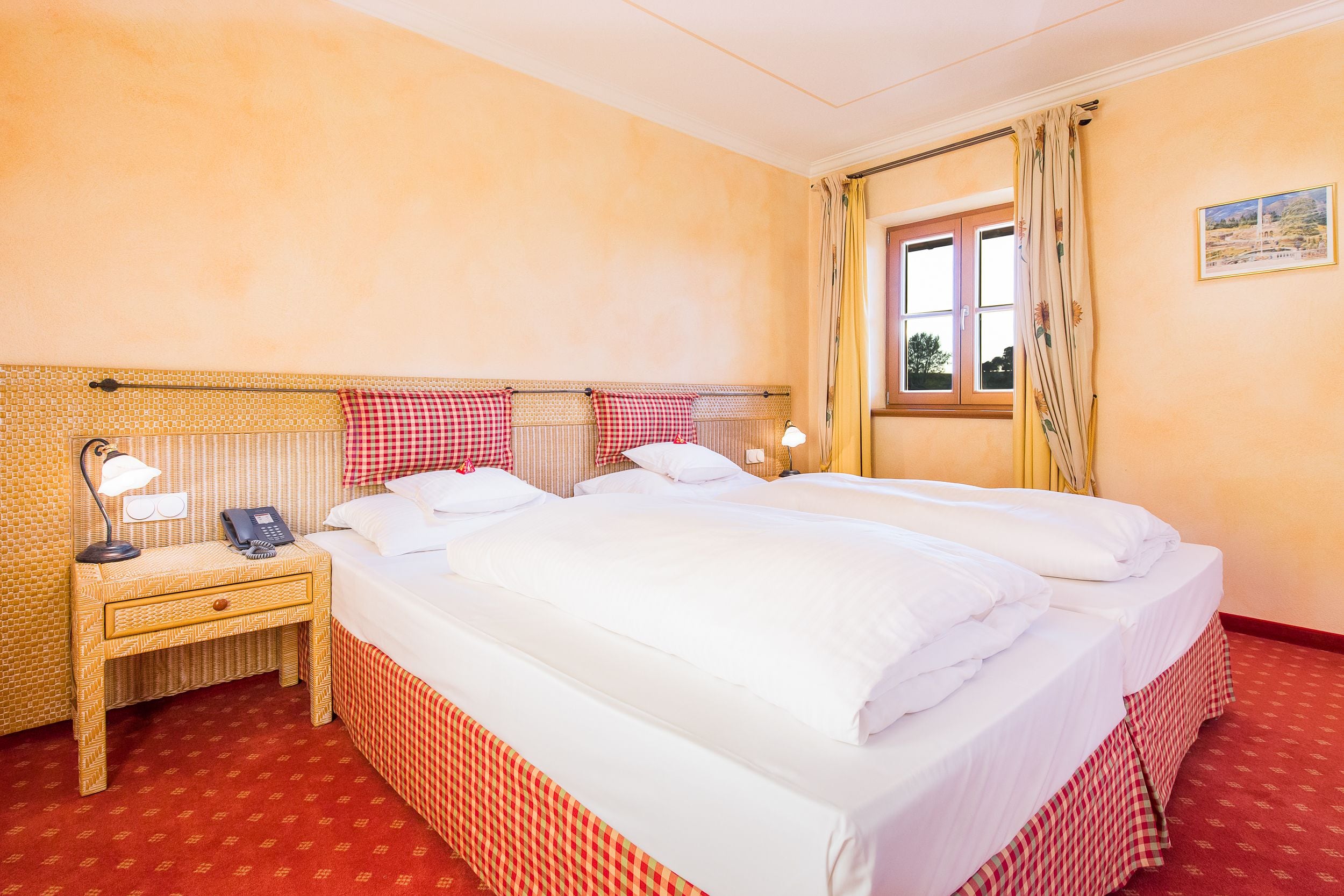 Een hotelkamer met een groot bed, een nachtkastje met een lamp, een telefoon en een raam met gordijnen.