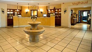 A lobby with a central fountain, a reception desk, and a sign reading "Voghhausl". - Hotel und Landgasthof Altwirt (Holzkirchen)