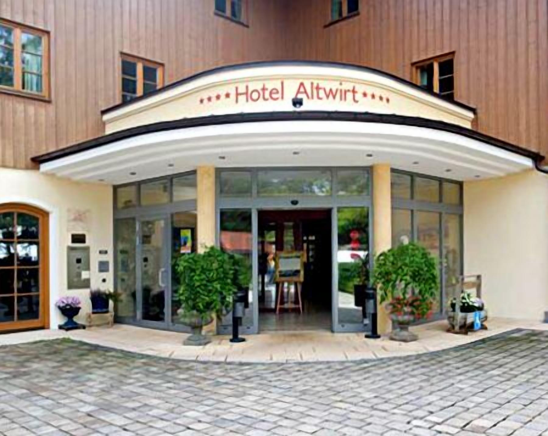 Entrada de hotel con techo curvo, puertas de cristal y plantas en macetas.