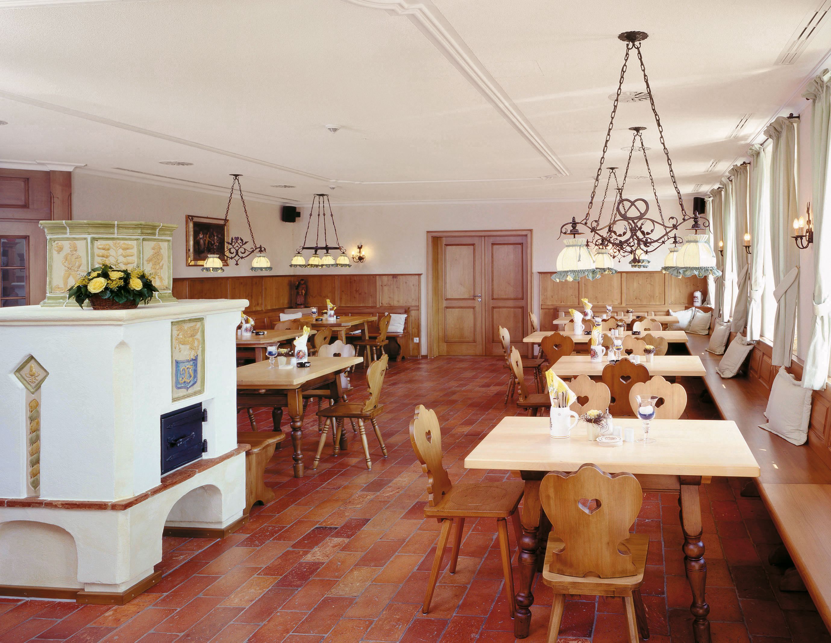 A dining area with wooden tables and chairs, a white fireplace, and hanging chandeliers.