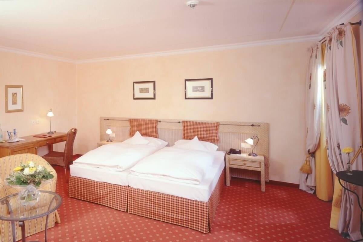 A hotel room with a large bed, a desk, a chair, and a small table with a vase of flowers.