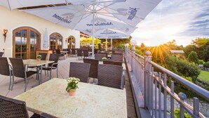 An outdoor patio with wicker furniture, large umbrellas, and a view of the countryside. - Hotel und Landgasthof Altwirt (Holzkirchen)