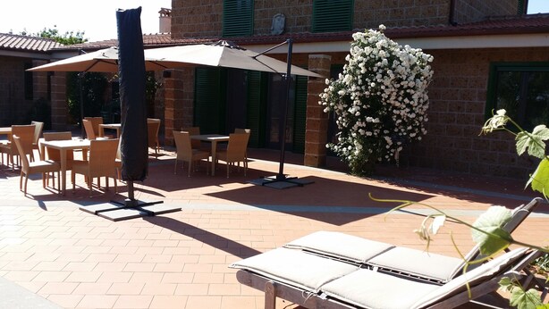 Un patio con mobiliario exterior, incluyendo sillas y mesas, y una zona cubierta con sombrilla.