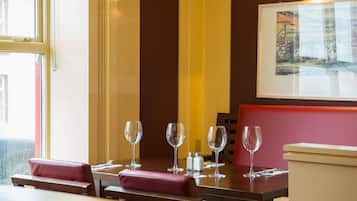 A restaurant interior with a table set for four, including wine glasses and cutlery, and a bench with a cushion.