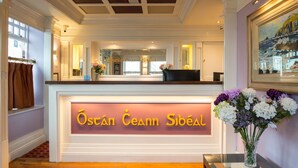 Un área de recepción con un cartel que dice "Óstán Ceann Síbéal" y un florero con flores sobre una mesa.