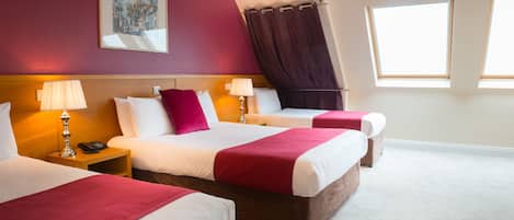 A hotel room with two beds, a painting on the wall, a window with curtains, and a lamp on the nightstand.