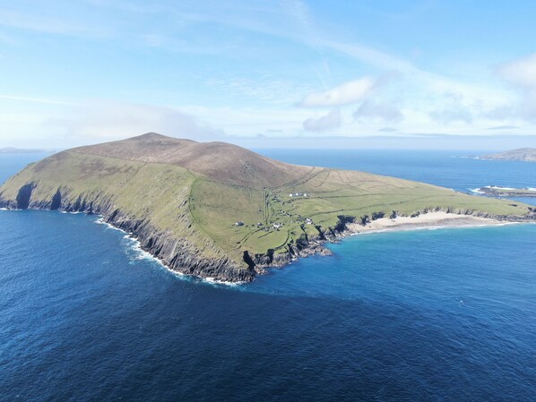 Vista aérea de una isla costera con un pequeño asentamiento, costa rocosa y mar azul cristalino.