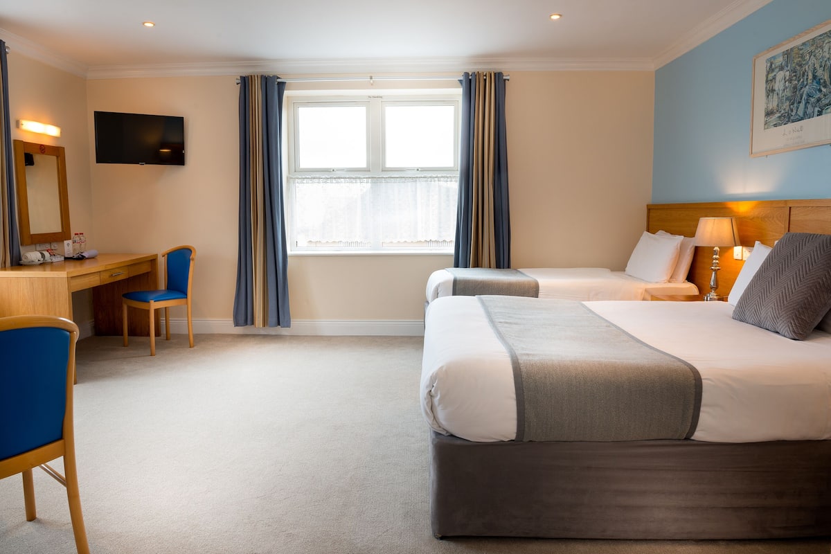 A hotel room with two beds, a desk, a chair, a television, and a window with curtains.