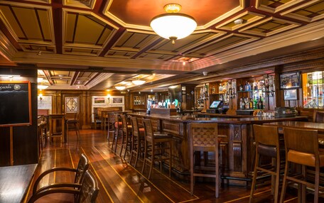 Zona de bar con suelo de madera, taburetes y una barra con varias botellas y una caja registradora.