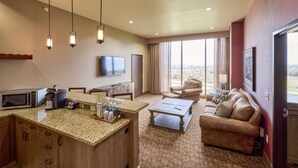 A hotel room with a kitchen area, a living room with a sofa and a coffee table, a flat-screen TV mounted on the wall, and a large window offering a view. - Choctaw Casino & Resort Pocola, Trademark Coll by Wyndham (Pocola)