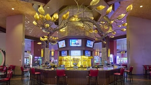 A bar area with a central counter, multiple screens, and red bar stools. - Choctaw Casino & Resort Pocola, Trademark Coll by Wyndham (Pocola)