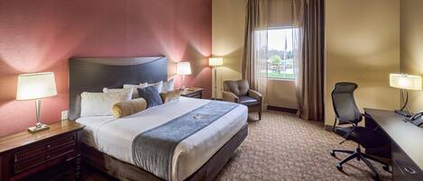 Une chambre d’hôtel avec un grand lit, deux tables de chevet avec des lampes, un bureau avec une chaise et une vue sur un parc depuis la fenêtre.