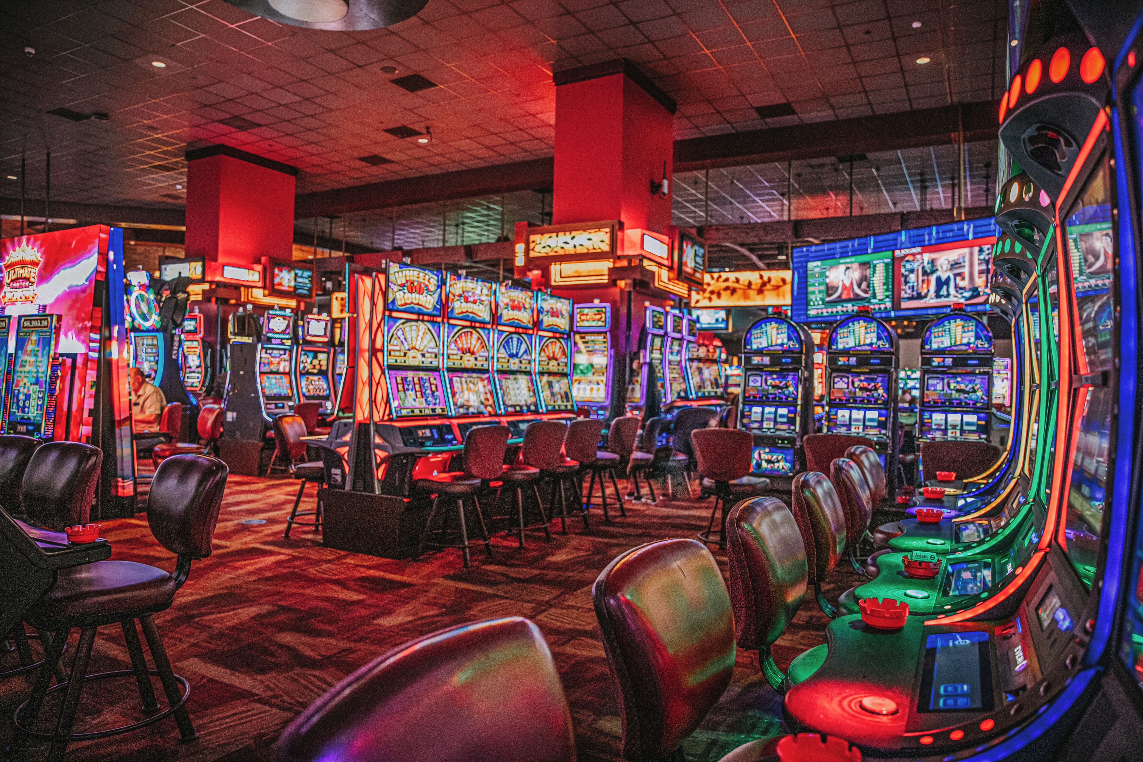A casino with multiple gaming machines, chairs, and a carpeted floor.